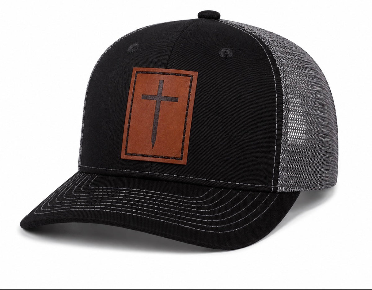 Black and gray trucker hat with brown leather cross patch, angled front view – ETRNL Apparel Cornerstone Hat
